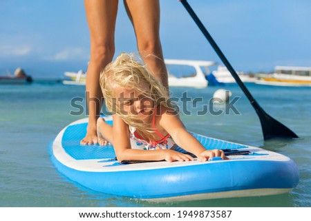 Active paddle boarder at sunset sea. Young mother with little clild paddling on stand up paddleboard. Healthy lifestyle. Water sport, SUP surfing tour in adventure camp on family summer beach vacation