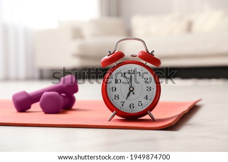 Alarm clock, yoga mat and dumbbells on wooden floor indoors. Morning exercise Royalty-Free Stock Photo #1949874700