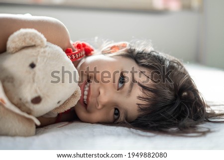 cute little asian girl sleep and hug teddy bear and cute smile on bed in the bedroom on a bright morning