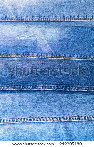 Denim texture, jeans in a line, vertically background of variety of comfortable casual pants and clothes. Light blue surface of cotton fabric with orange thread seam and stitches. Copy space backdrop.