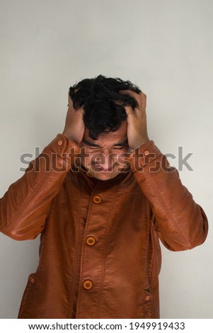 picture of angry and irritated man holding his hair in anger wearing brown leather coat in isolated white background.