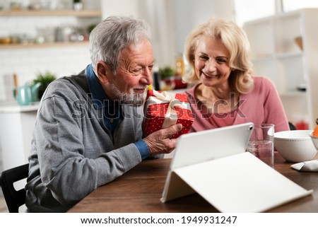 Senior couple having video call. Happy husband giving his wife a gift