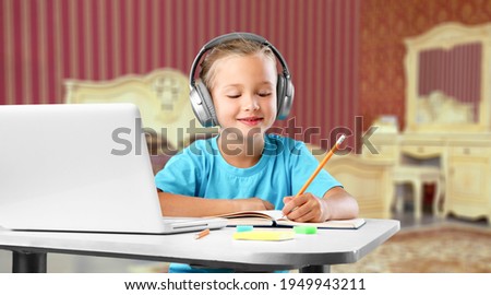Smiling little child wearing headphones sitting at the table, studying at home,