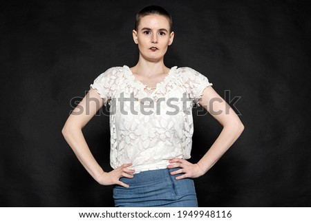 Young Woman with Hands on Hips and white lace top and jean skirt against a black background