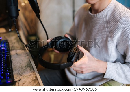 Closeup of man wearing headphones during the work with music at home. Background of micrphone and pc with keyboard. Neon light