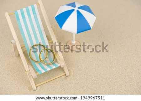 Two golden wedding rings close up on a sun lounger on sand. Wedding on the beach invitation card concept.