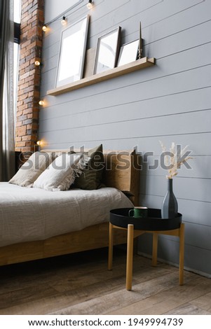 A modern white ceramic vase with dried grass and a cup of coffee or tea beside the double bed. Grey bed linen and pillows in the bedroom, Scandinavian interior.