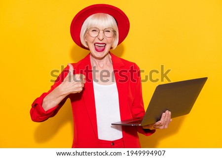 Photo portrait of old lady wearing red suit keeping laptop showing thumb-up sign isolated vibrant yellow color background