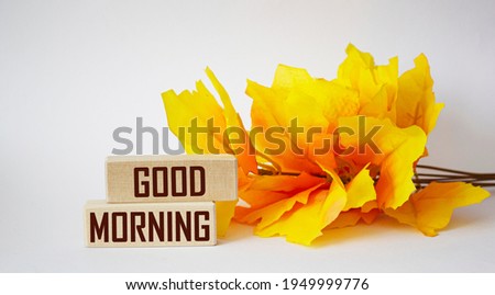 Good morning written on wooden blocks and white background with yellow foliage