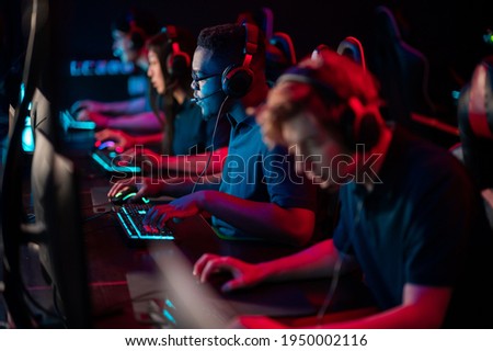 A multi-racial team of esports athletes conducts a training session before an online shooter tournament. Neon light. Royalty-Free Stock Photo #1950002116