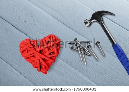 Pano picture with a heart made of threads and nails on a wooden board lies next to a hammer and nails