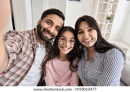 Happy indian couple and teen daughter taking selfie looking at phone camera. Smiling family with child girl making picture or having virtual call meeting, shooting vlog on modern smartphone at home.