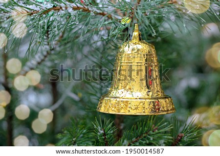 Christmas background with a golden bell on a spruce branch, holiday lights and snow on a street Christmas tree