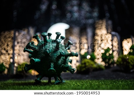 Cartoon style city buildings. Realistic city building miniatures with lights. Big Corona virus miniature in the city at night. Stay home stay safe or coronavirus pandemic concept. Selective focus.
