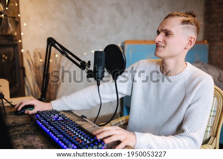 Young man makes a podcast audio recording at home. Man using pc and two professional microphones. Person recording a podcast at home using microphone and computers. Recording online podcast