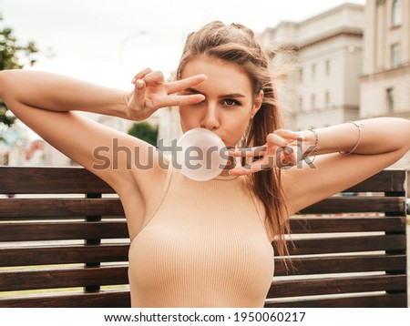 Portrait of young playful hipster female.Model blowing bubble with chewing gum. Woman looking at camera.Female in sunglasses posing in the street at sunny day.Shows peace sign and going crazy
