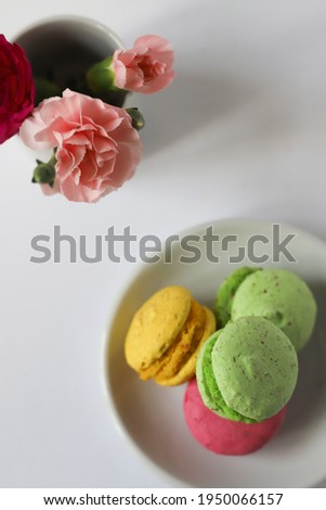 a lot of sweet tasty macaroon desserts in purple pink yellow and green lie on a white background next to flowers in a white cup in pink and purple. for screensavers labels flyers banners invitations
