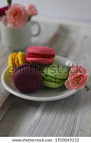 many sweet tasty macaroon desserts in purple pink yellow and green lie on a wooden surface next to flowers in a white cup in pink and purple. for screensavers labels flyers banners invitations