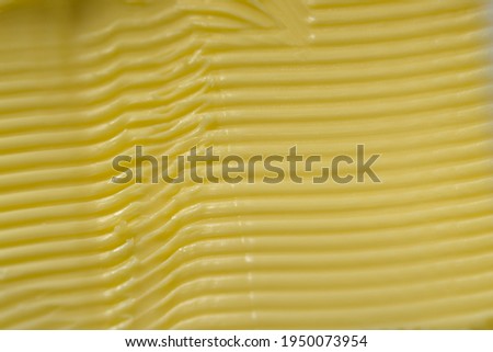 Super macro image of spreadable yellow margarine, after having a kitchen knife run through it to create a texture of horizontal grooves and ridges