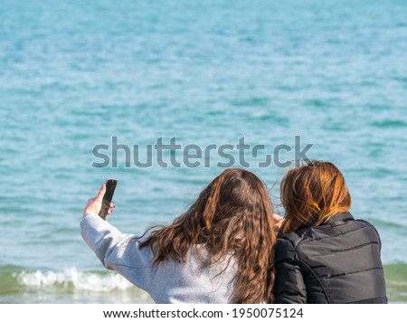 Two girls friends sitting and taking a selfie at the edge of the sea. Girls relaxing