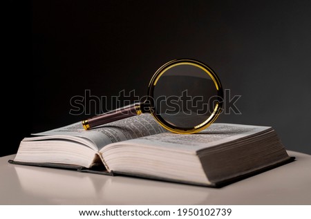 Open book closeup with turning pages and magnifying loupe. Textbook in hard cover on table. Studying and research concept. Royalty-Free Stock Photo #1950102739