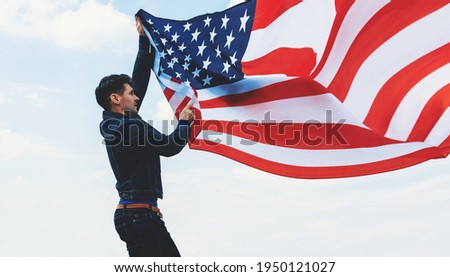 man waving american USA flag against cloudy blue sky	