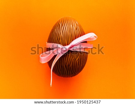 Chocolate Easter egg with pink ribbon on orange background. Spring holidays concept