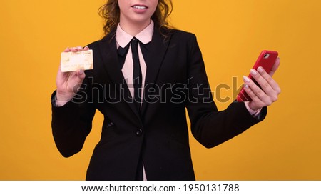 young woman posing isolated over yellow wall background using mobile phone holding debit card.