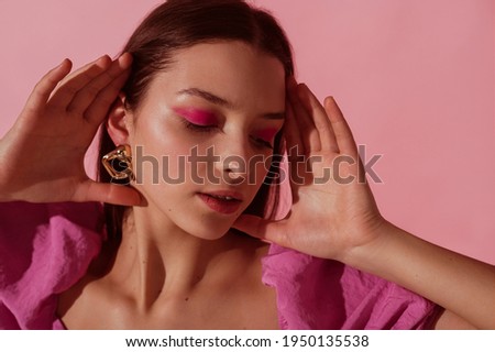 Close up beauty portrait of young beautiful woman with pink, fuchsia color eyeshadow makeup, flawless clean skin, wearing elegant golden earrings, pink blouse. Spring, summer fashion trend Royalty-Free Stock Photo #1950135538