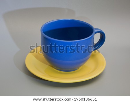 Blue teacup on a yellow plate with shadow on gray plain background