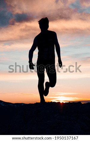 VERTICAL IMAGE OF A PERSON RUNNING AT THE TOP OF A MOUNTAIN. MAN ENJOYING AND HAVING FUN DURING SUNSET. OUTDOOR AND SUNSET CONCEPT.