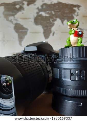 Decorative figurine of a crocodile with a camera standing on an inverted lens near the camera against the background of a blurred world map