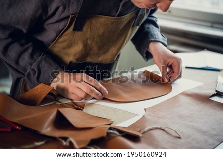 A talented young guy helps his father in the family business, cuts out blanks for shoes from leather Royalty-Free Stock Photo #1950160924