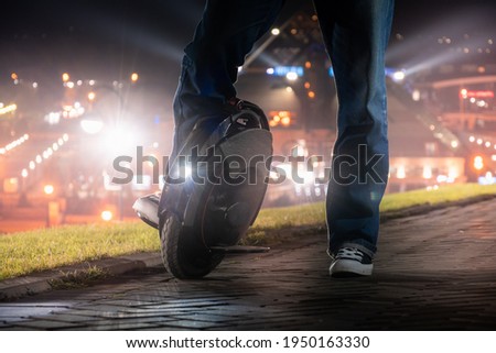 A man on an electric mono wheel stopped while driving around the city. Night riding on an electric unicycle (EUC) with a bright headlight. Royalty-Free Stock Photo #1950163330