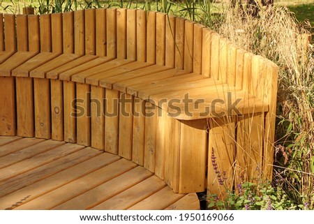 Wooden Patio with Wooden Rounded Bench. Designed Garden Surface. Landscaped Garden with Wooden Elements. Small Decorative Garden. Designed Patio or Terrace. Hardwood Decking or Flooring.