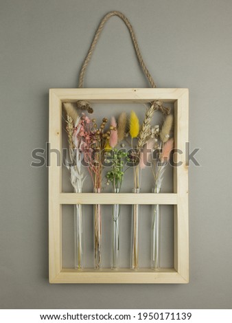 Arrangement of dried flower  in narrow glass vases in a natural wooden frame with handle. Pink, yellow, beige, white colors. Grey background