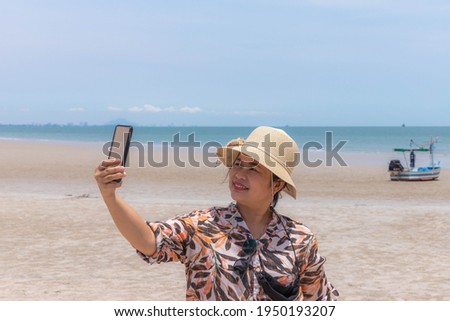 A girl using the phone Take a picture of selfie with a fishing boat moored by the beach.