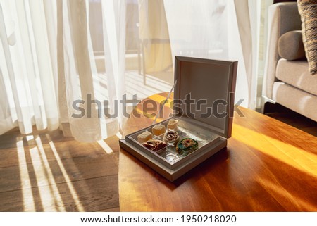 Modern room interior with an open window in minimal style. Transparent tulle with morning sun rays on shadow background. Box with oriental sweets on table