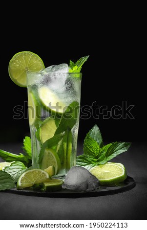 Fresh homemade mojito cocktail in a tall glass with lime, mint and ice on a black background, copy space, vertical image
