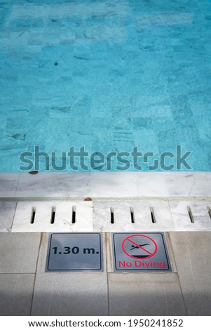 "No diving" metal sign plate at swimming pool side, with blurred background of clearly blue water in the pool. Sign and symbol photo in sport recreation location.