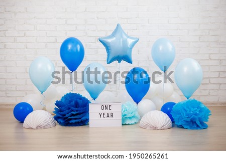 baby boy first birthday party decoration - air balloons, paper balls and lightbox with one year text over white brick wall