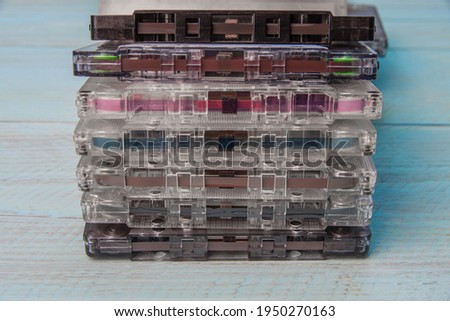 A stack of audio cassettes on a blue wooden background. You can see the magnetic film, rollers and a pressure mechanism with a felt pad. Close-up
