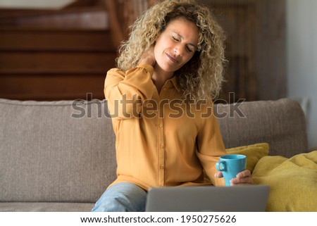 Tired young woman touch stiff neck feeling hurt joint back pain rubbing massaging tensed muscles suffer from fibromyalgia ache after long computer work study in incorrect posture sit on sofa at home Royalty-Free Stock Photo #1950275626