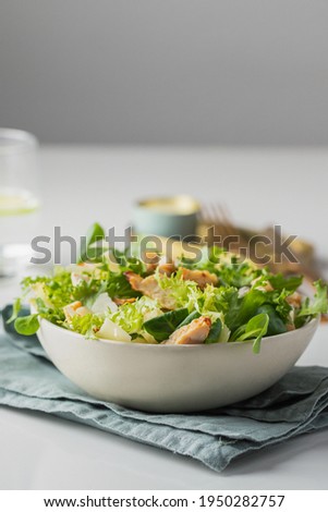 Healthy salad with  different lettuce, croutons,cheese,  chicken and dressing with especial sauce. Caesar salad in the white plate served with glass water and gold cutlery on the restaurant table. Royalty-Free Stock Photo #1950282757