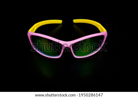 Children's glasses for cycling and sports. Made of pink plastic with yellow temples and UV-resistant lenses. Photographed on a black background.