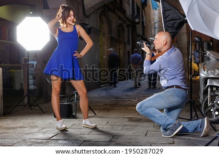 Professional photo shooting outdoors. Attractive happy positive smiling female model posing to photographer on city street
