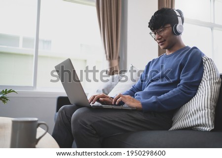 Young attractive man sitting on  sofa wearing headphone movie at home.