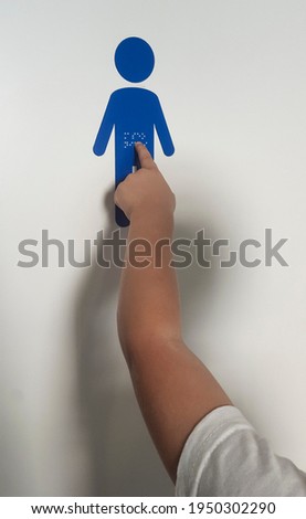 Child boy touching braille sticker sign at children toilet door. Blind children accessibility concept