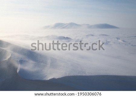 Winter Arctic landscape. View of the snow-covered tundra and snow-covered mountains. Very cold and windy weather. Blowing blizzard. Chukotka, Siberia, Russia. Low depth of field, blurred background.