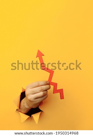 Hand with a red arrow up through a yellow paper hole. Vertical image